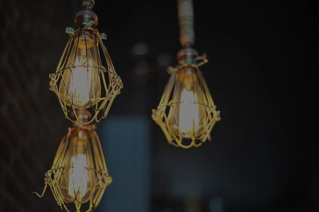 Three industrial pendant lights with glowing Edison bulbs and metal cages.