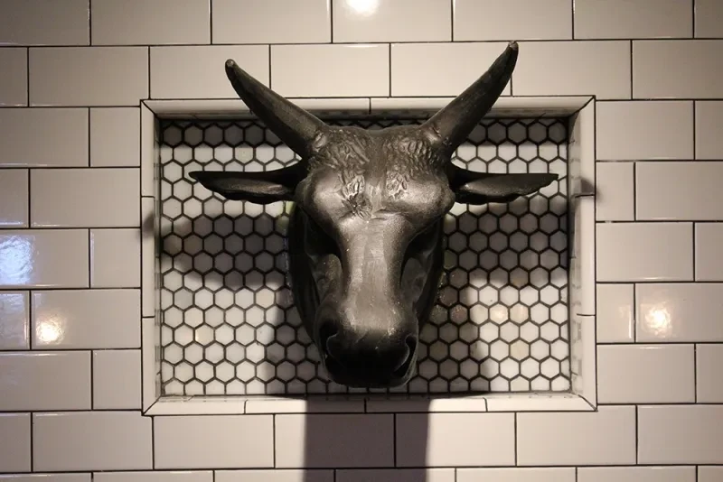 Dark metallic bull's head sculpture in a hexagonal and subway tiled niche.