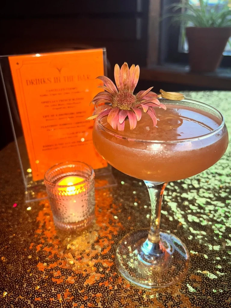 Warm amber cocktail in coupe with dried flower on shimmering gold table.