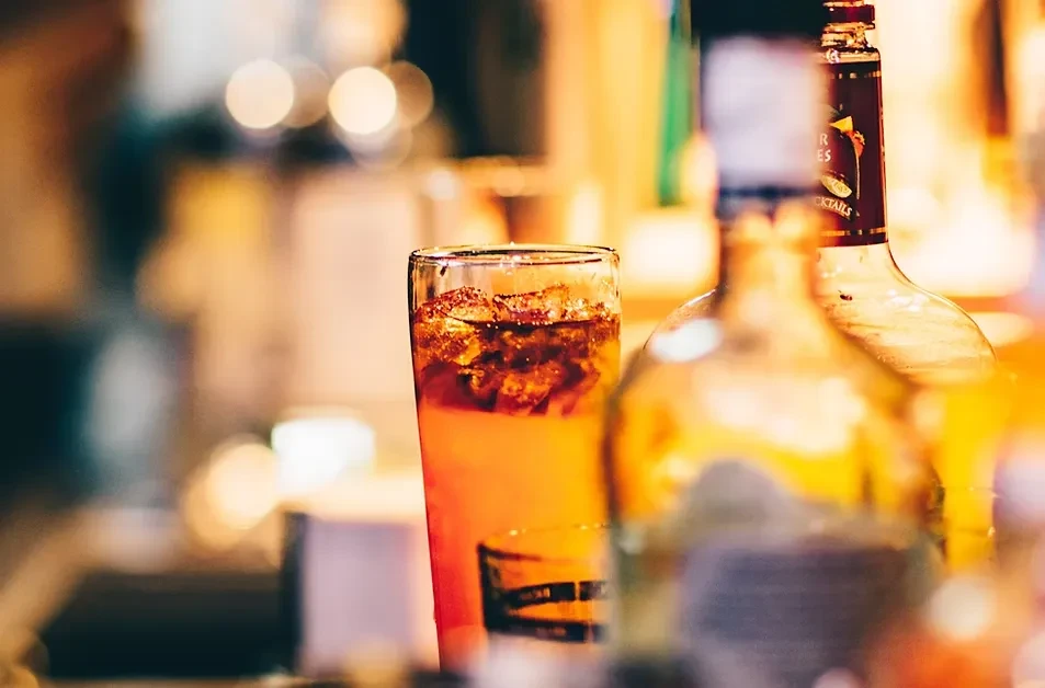 Amber drink in glass with ice on bar counter, blurred bottles.