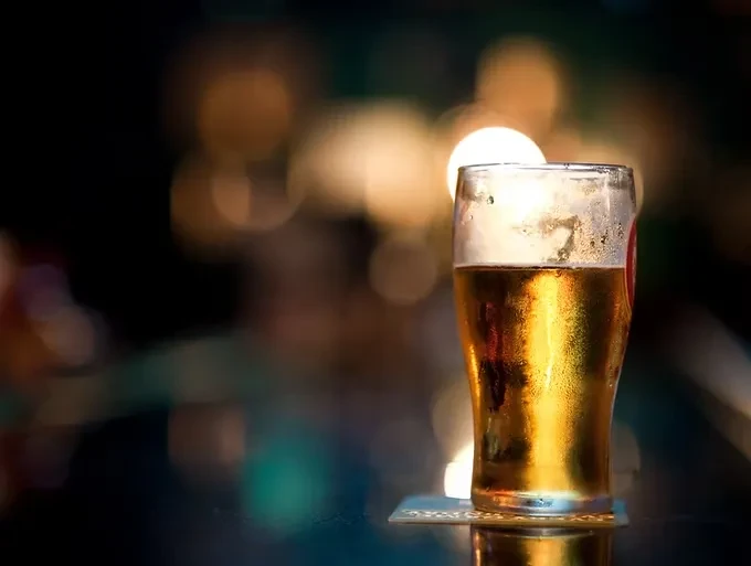 Chilled golden beer glass with condensation on a dark bar.