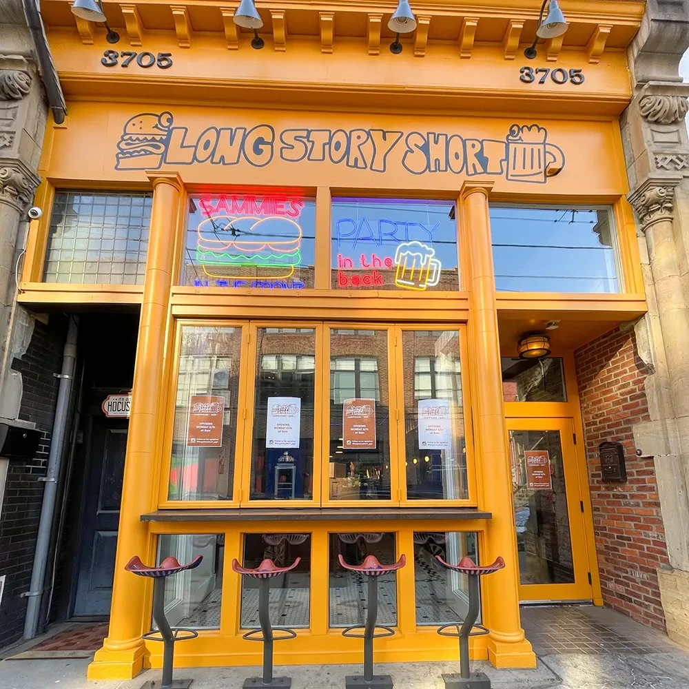 Bright yellow "Long Story Short" restaurant with burger, beer, and "OPENING SOON" signs.