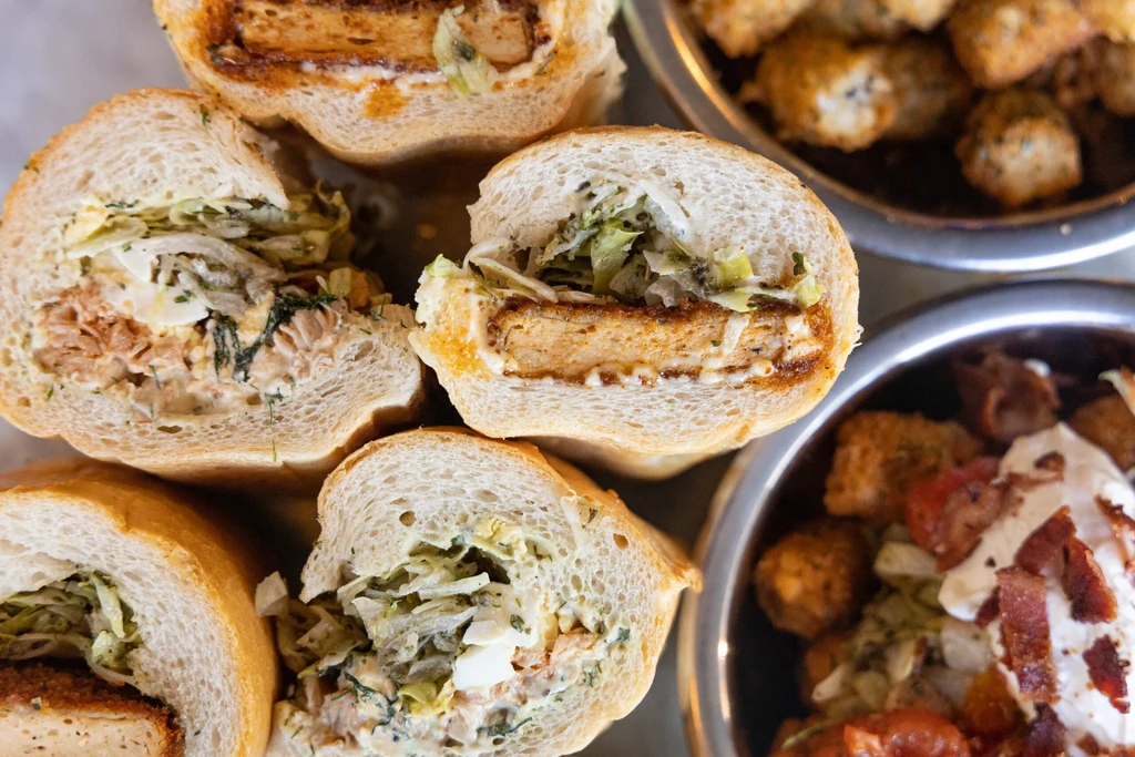 Overhead view of various halved sandwiches with protein fillings and side dishes.