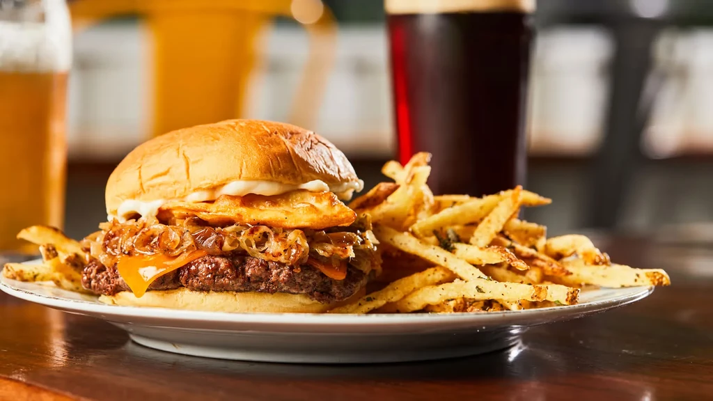Plate with gourmet burger, fries, and two drinks in a restaurant.