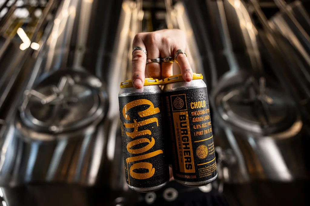 Chilled Cholo beer cans held by hands in a brewery.