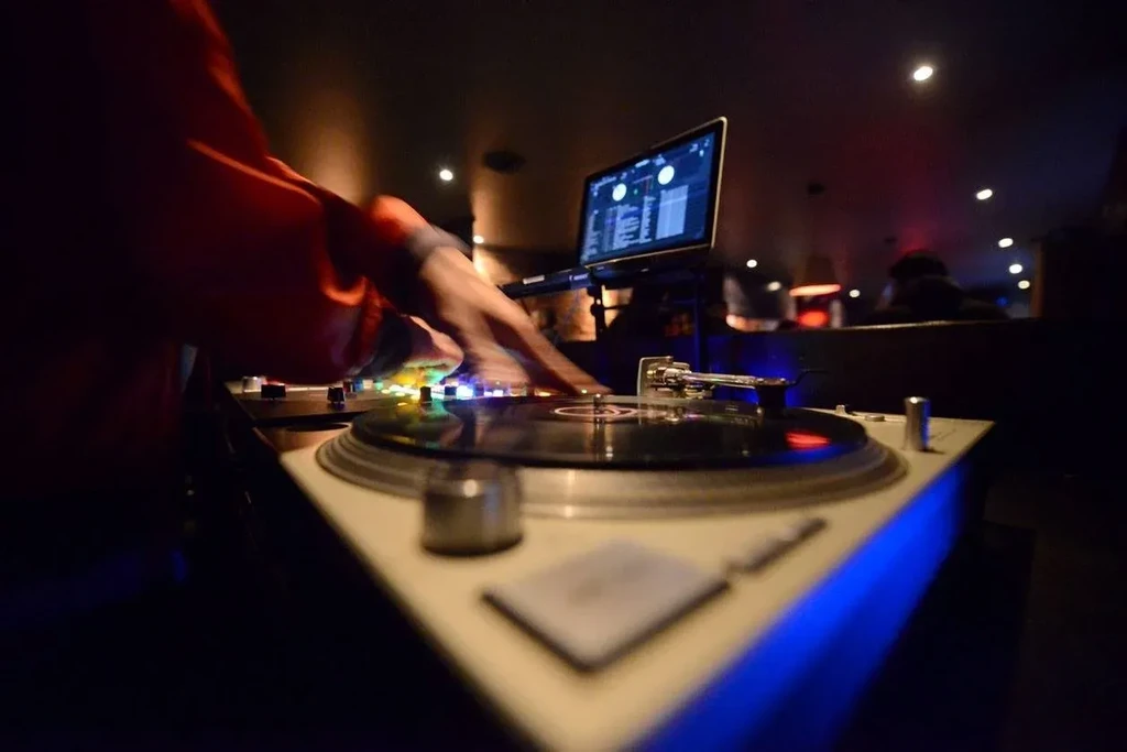 DJ's hands operate illuminated turntable and mixer in a dark venue.