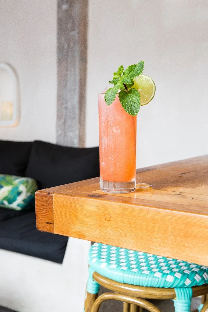 Reddish-pink cocktail with mint and lime on a wooden table.