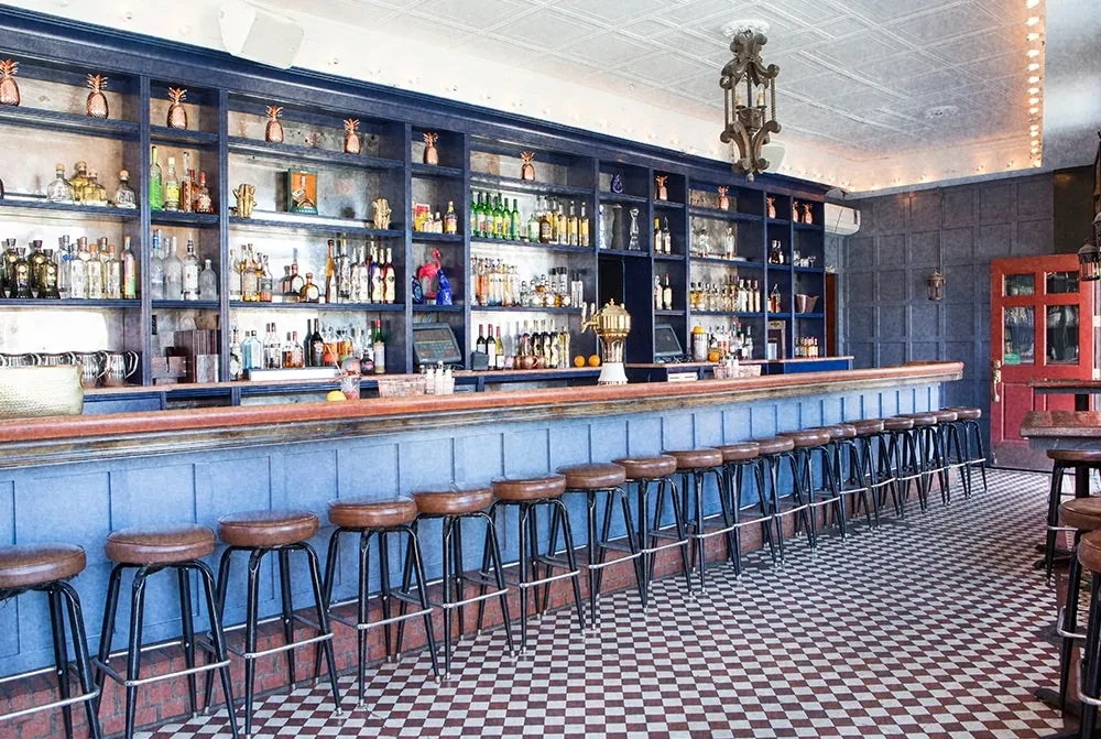 Empty classic bar with dark blue counter, bottles, and stools.