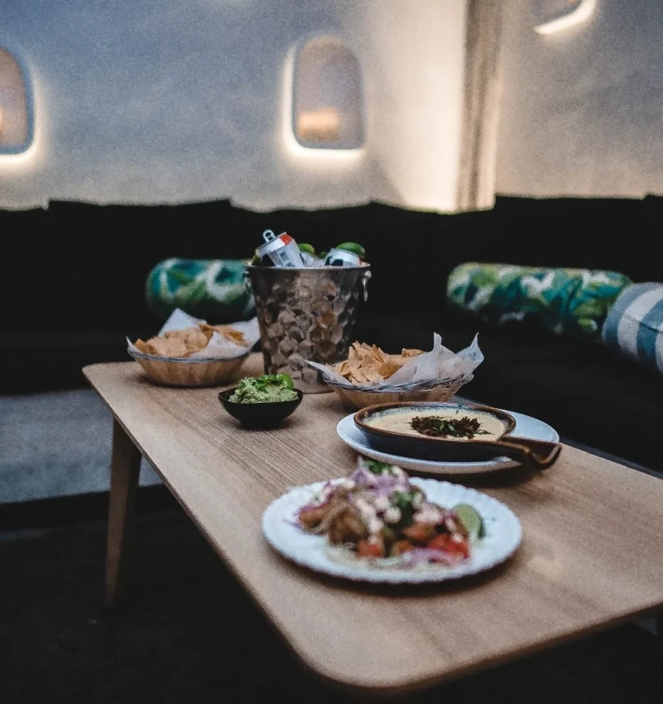 Food and drinks on a wooden table in a dimly lit lounge.