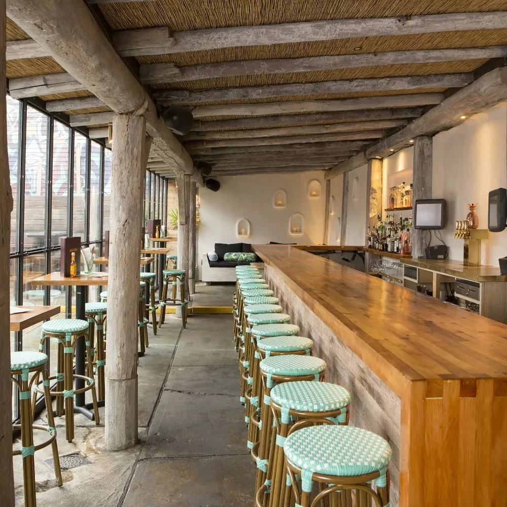Empty rustic bar with thatched ceiling and mint green stools.