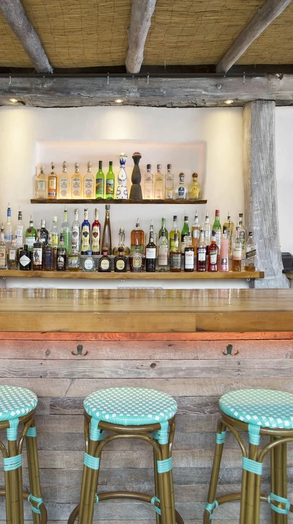 Well-lit bar with liquor bottles on shelves and three woven stools.