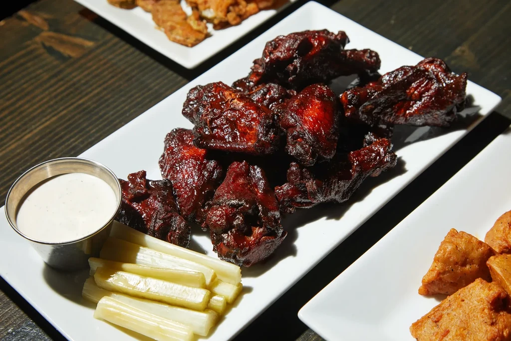 Glossy chicken wings, dipping sauce, and celery on a dark wooden table.