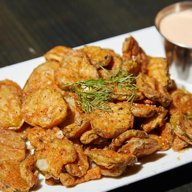 Plate of golden-brown fried pickles with dill and pink dipping sauce.