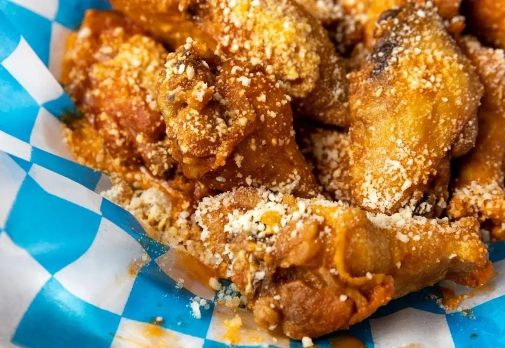 Golden brown sauced chicken wings with Parmesan in a checkered basket.
