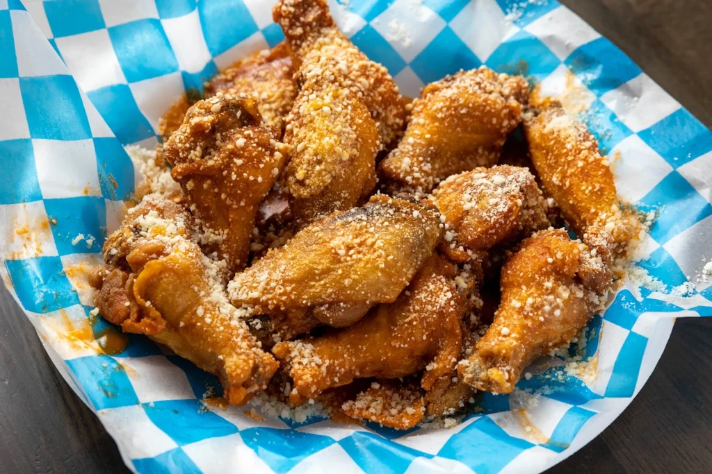 Golden-brown chicken wings with cheese and red sauce in a basket.