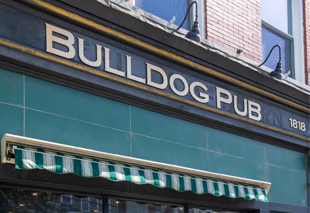 BULLDOG PUB gold sign above teal tiles and a striped green awning.