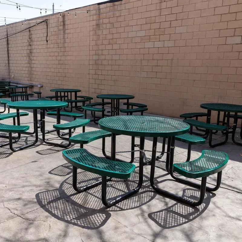 Green perforated metal picnic tables on a sunny concrete patio.