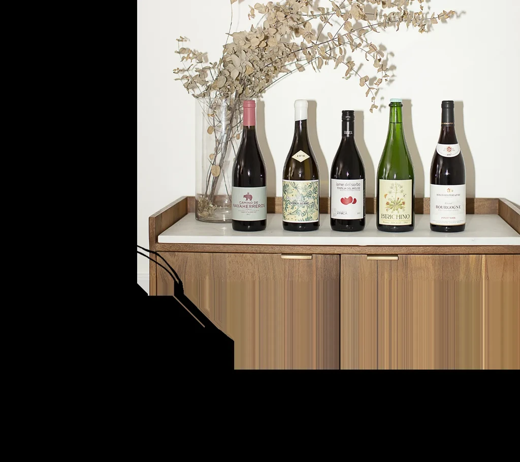 Five different wine bottles, dried eucalyptus, on marble and wood cabinet.