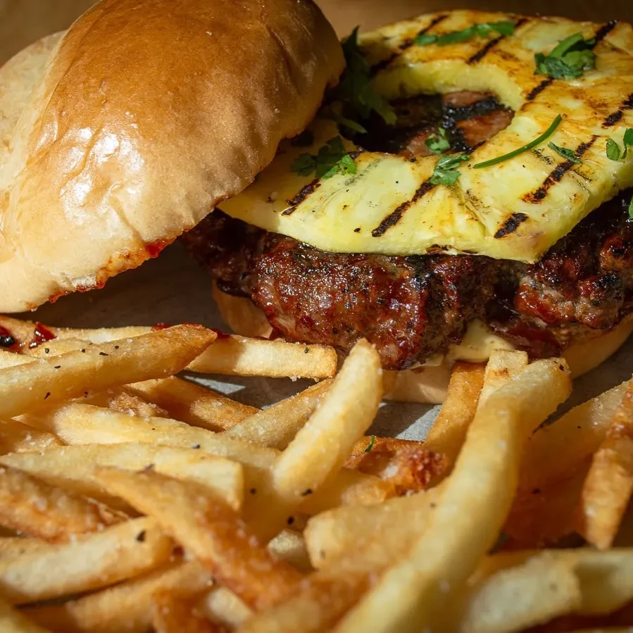 Close-up of burger with grilled pineapple, herbs, and golden fries.