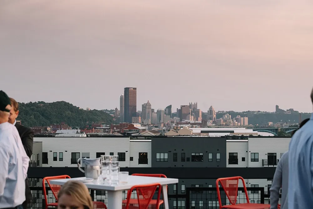 Rooftop bar overlooking Pittsburgh skyline at dusk.