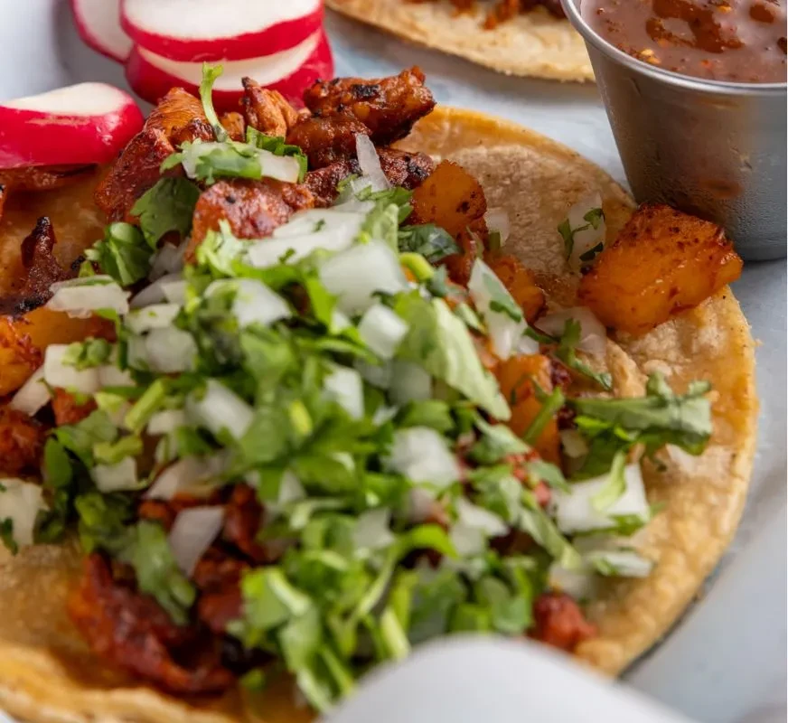 Close-up of an al pastor taco with onions, cilantro, radish, and salsa.