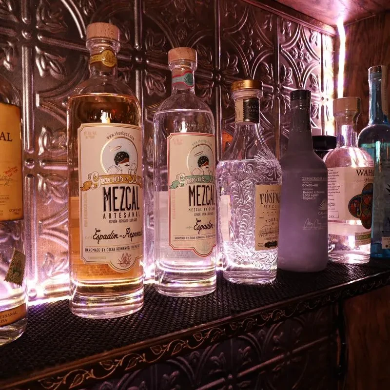 Various Mezcal and spirit bottles illuminated by purple and pink light.