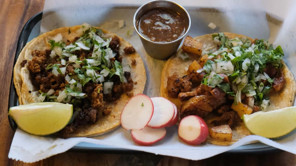 Two street tacos with ground meat and pork, salsa, radish, and lime.