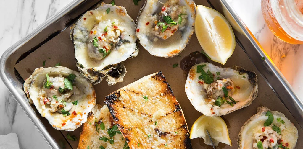 Close-up of baked oysters with creamy sauce, toast, and lemon.