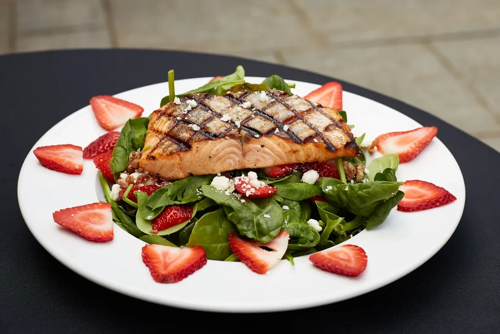 Grilled salmon fillet on spinach salad with strawberries, cheese, and nuts.