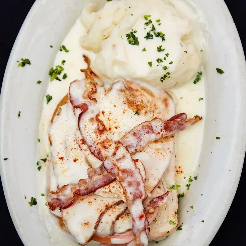 Oval dish with creamy chicken, crispy bacon, mashed potatoes, herbs.