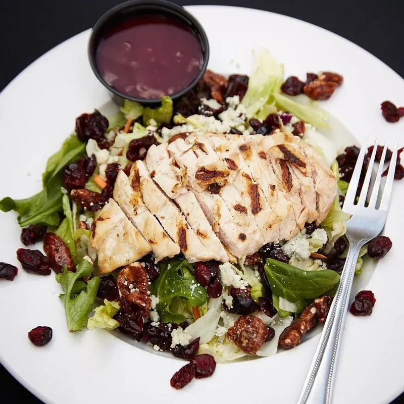 Overhead grilled chicken salad with blue cheese, cranberries, pecans, and dressing.