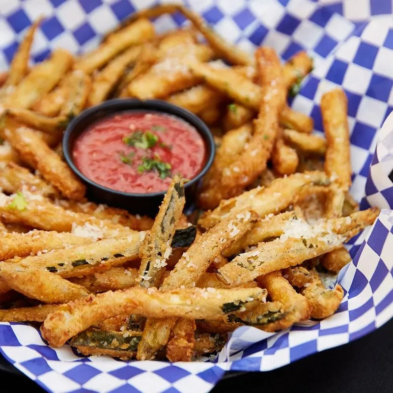 A basket of crispy fried zucchini sticks with Parmesan and red sauce.