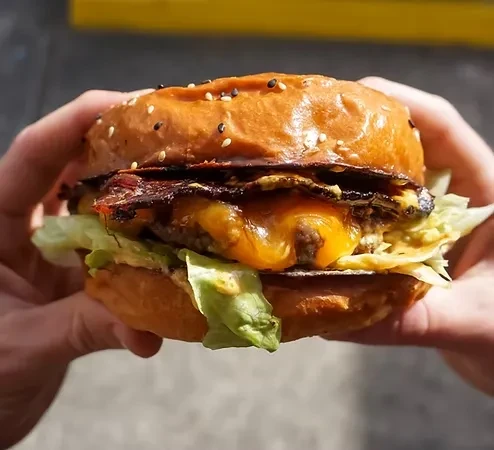 Gourmet burger with melted cheese, bacon, lettuce, held in hands.