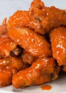 Close-up of a pile of buffalo wings with vibrant orange, glossy sauce.