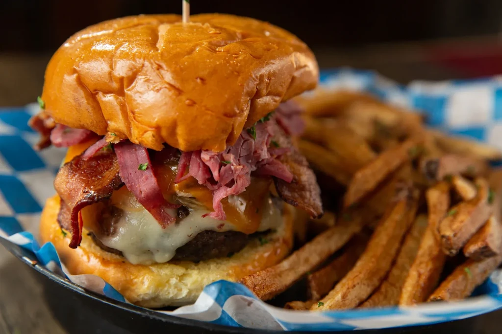 Close-up of a gourmet burger with cured meat, cheese, bacon, and fries.