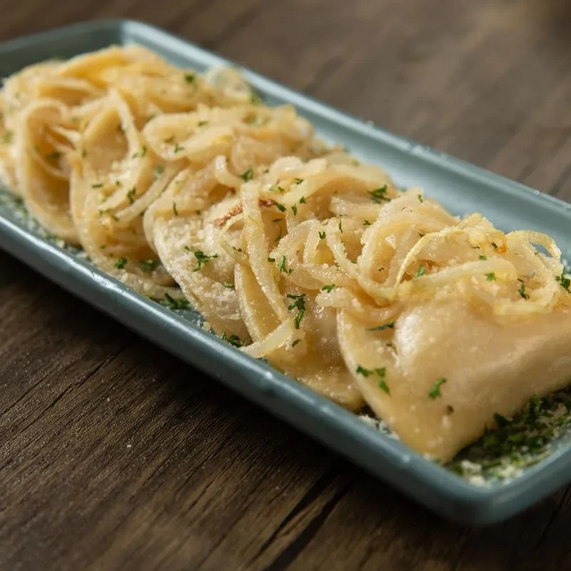 Pierogi topped with caramelized onions, green herbs, and cheese.