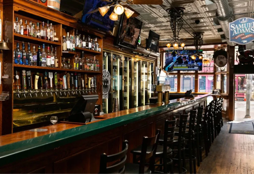 Traditional bar interior with wooden counter, liquor, beer taps, and TVs.