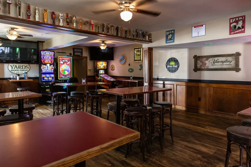Empty rustic bar interior with wooden tables, gaming machines, and beer decor.