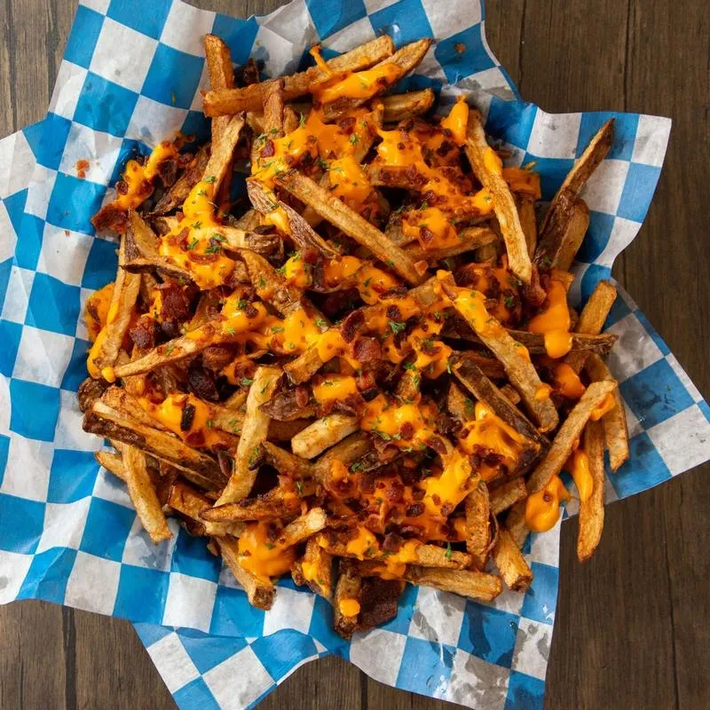 Loaded fries with cheese, bacon, and chives in a checkered basket.