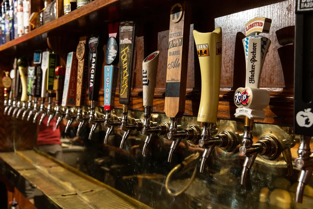 Row of unique beer tap handles and spirit bottles on a bar.