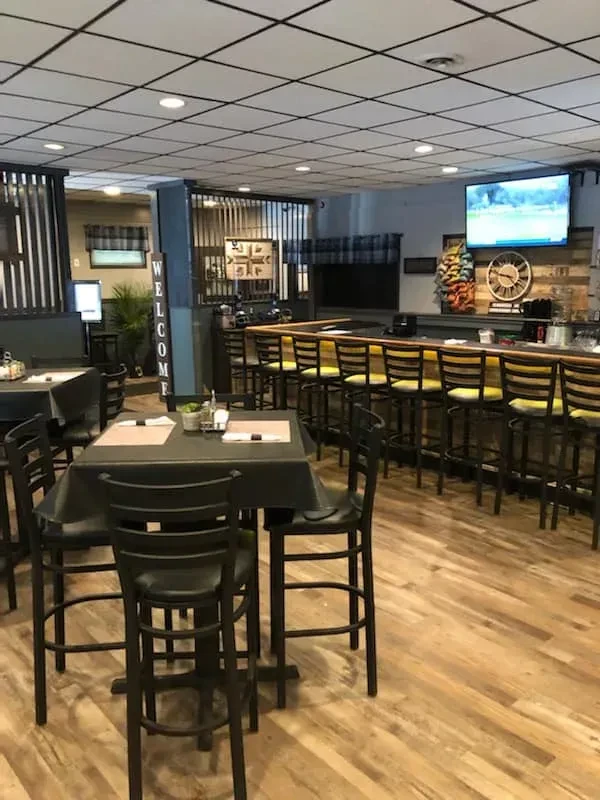 Empty casual restaurant interior with high-top tables and a long bar.