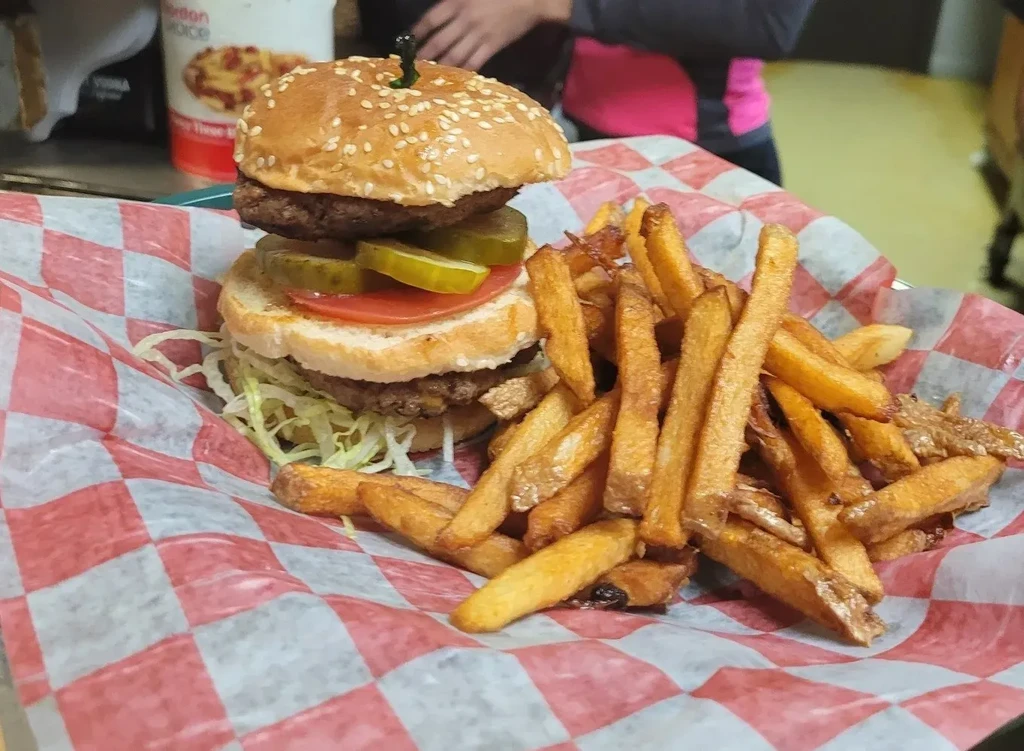 Double cheeseburger and golden fries on checkered paper in a basket.
