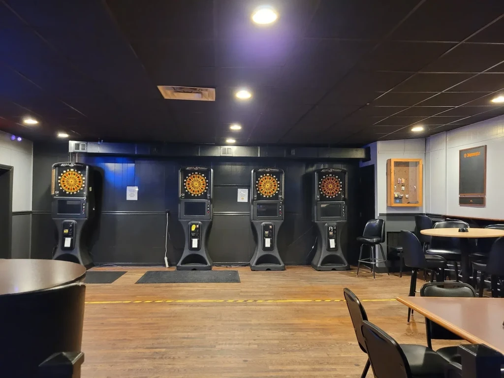 Empty bar interior featuring four electronic dart machines and seating.