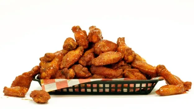 Glossy, reddish-orange chicken wings overflowing from a checkered basket.