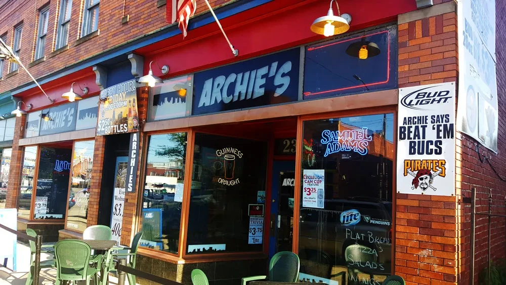 Archie's bar exterior: brick, red awning, large windows, outdoor seating.