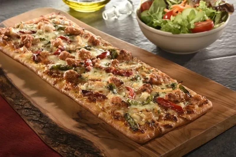 Rectangular flatbread pizza with chicken, bell peppers, and salad.