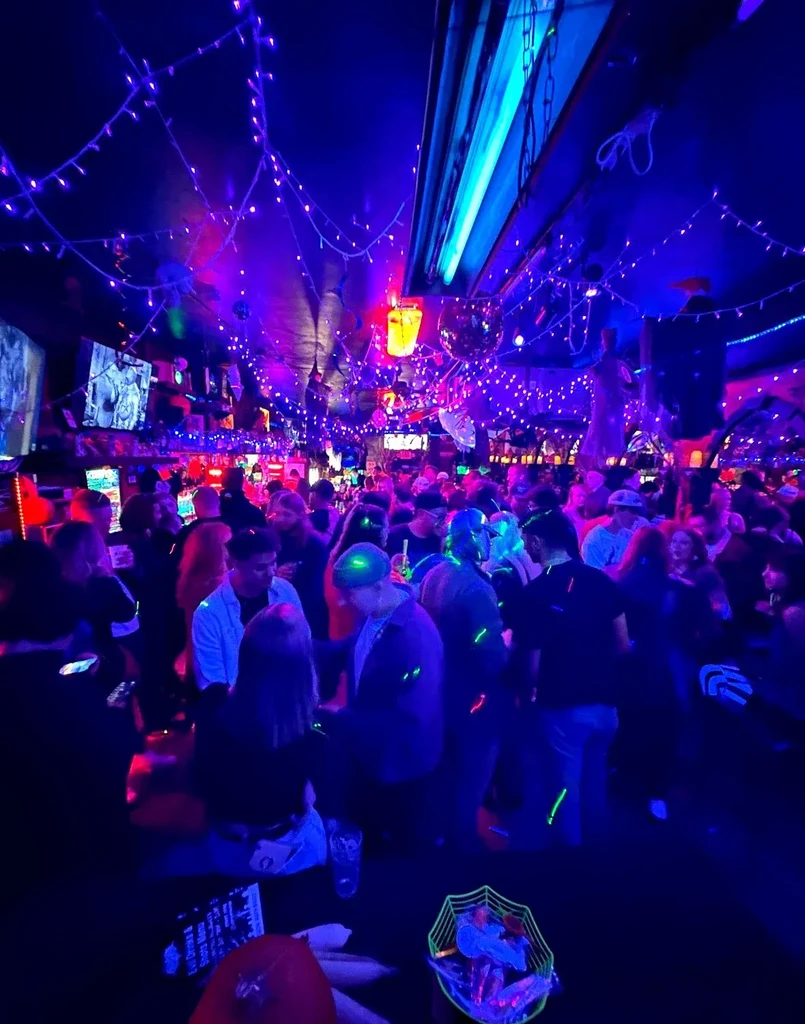 Crowded blue-lit nightclub, fairy lights, disco balls, people with glowing accessories.