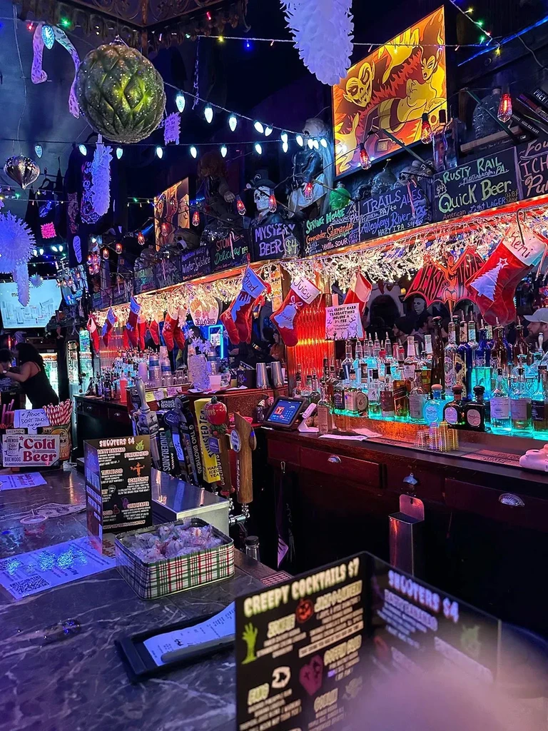 Dimly lit bar interior with horror decor, glowing bottles, and themed cocktails.