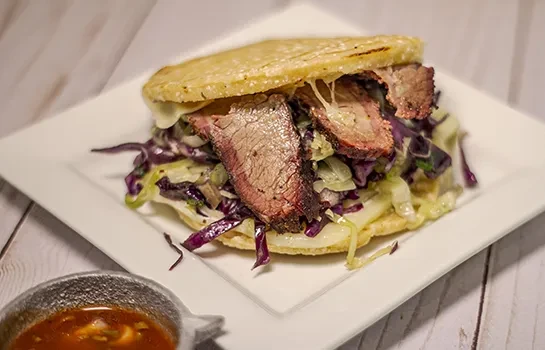 Close-up of brisket taco with cabbage, cheese, and dipping sauce.