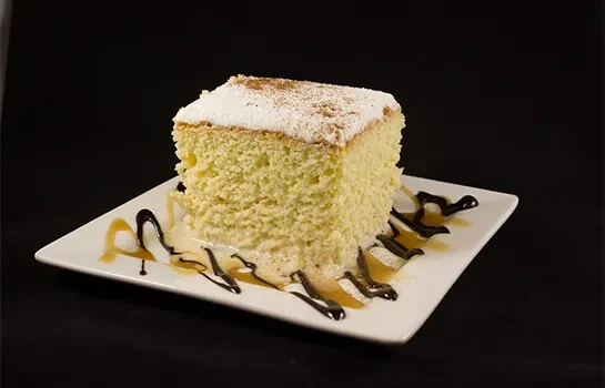 Slice of sponge cake with powdered sugar, chocolate, and caramel sauces.